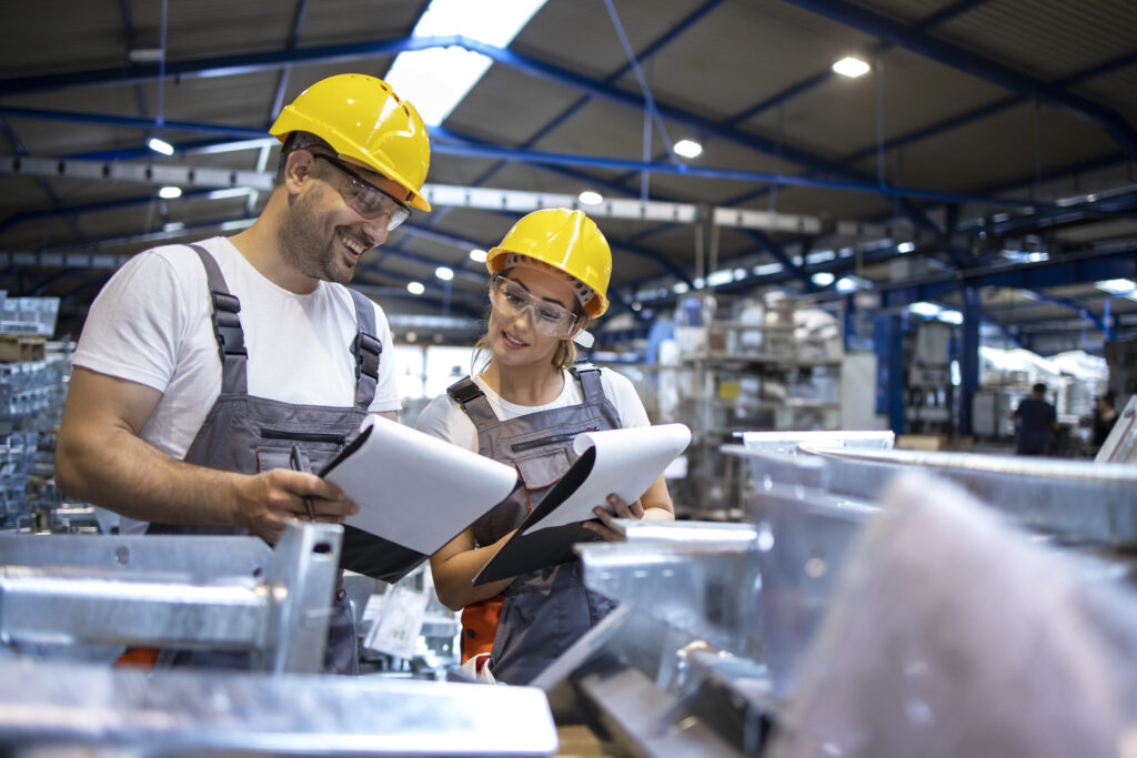Factory workers analyzing production results in large industrial hall.